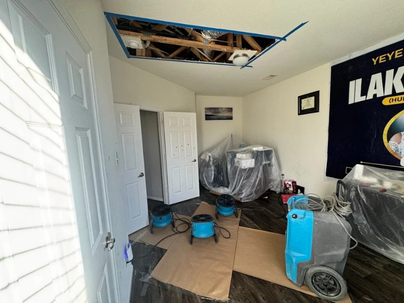Room with ceiling damage being dried by blue air movers and covered furniture.