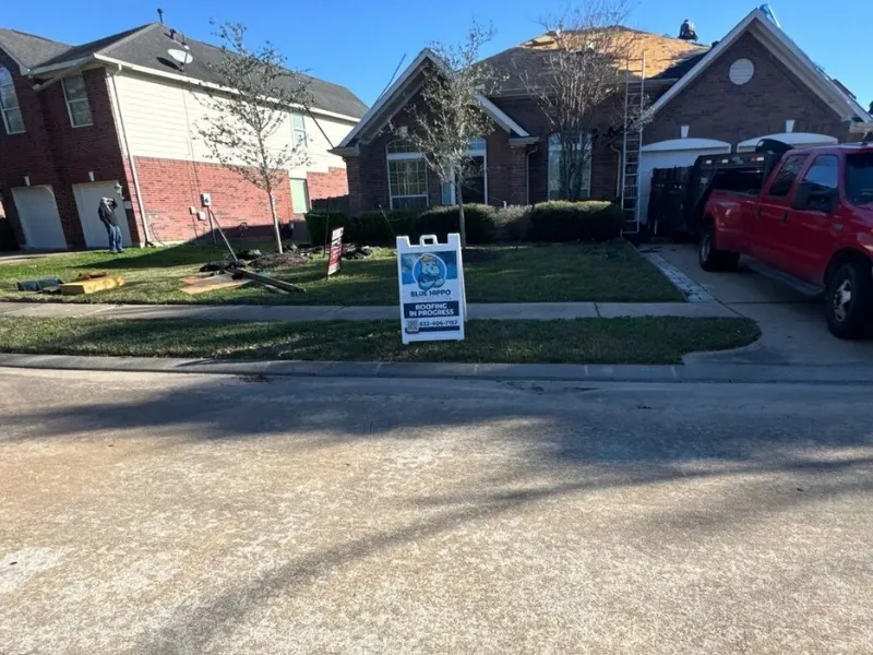 House with a roof under construction and a sign reading "Blue Hippo Roofing in Progress" on the lawn.