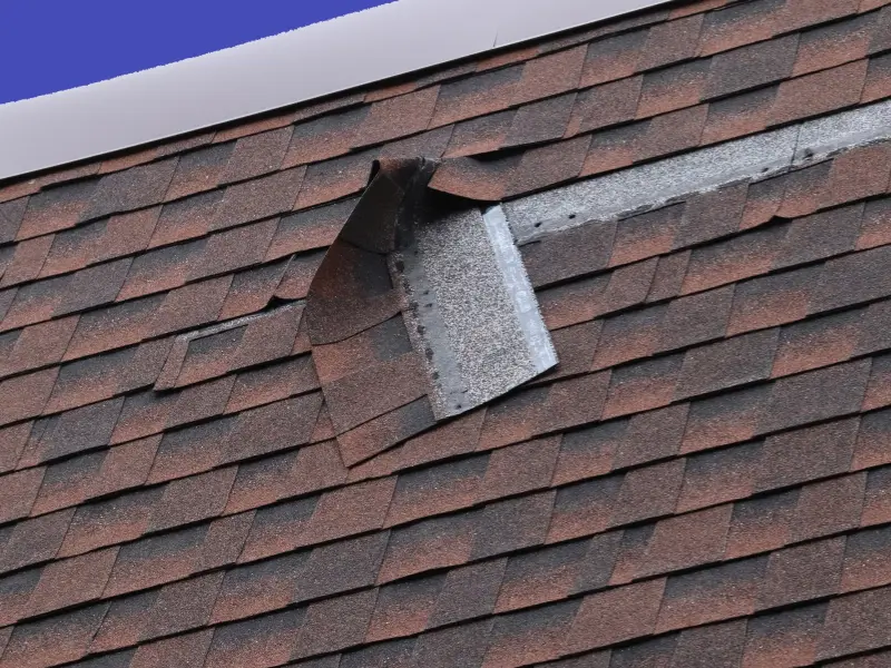 Roof shingles peeling away, exposing underlying metal flashing.