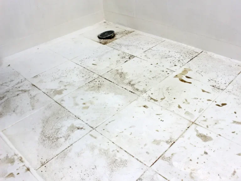 White tiled floor with dirt stains and a black drain cover in the corner.