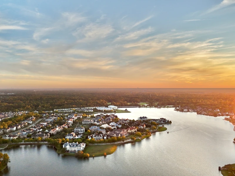 Aerial view of a lakeside residential neighborhood at sunset with houses and trees.