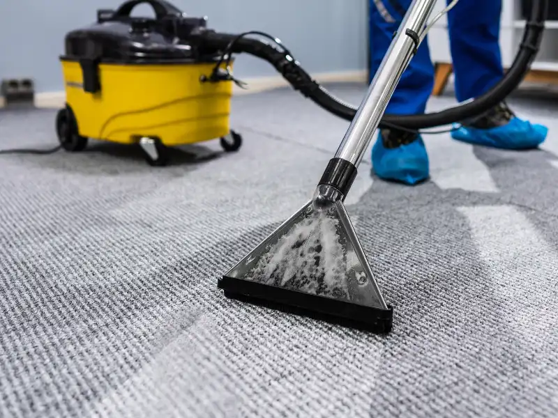 Carpet cleaning machine with a yellow vacuum and a person wearing blue shoe covers.