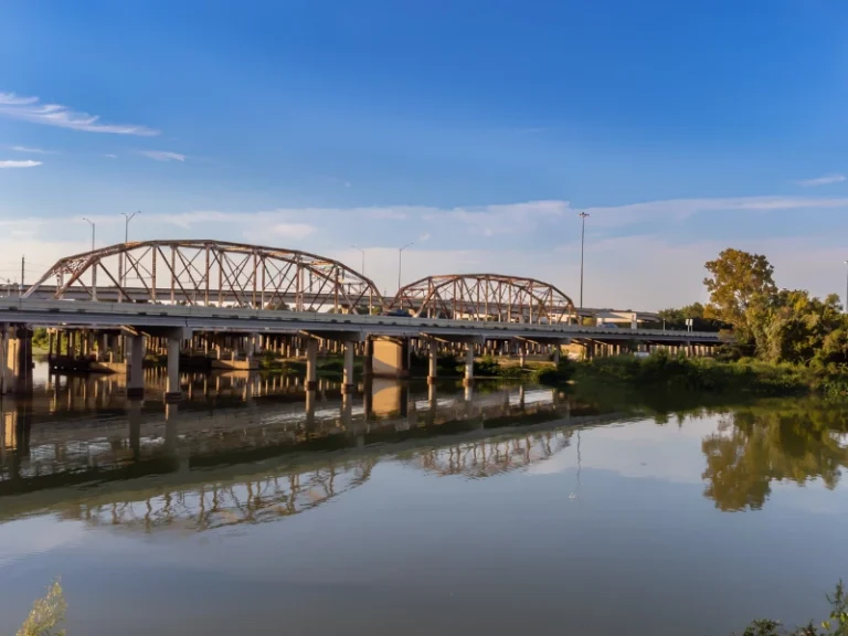 Two metal truss bridges over a river with clear sky and reflections in the water.