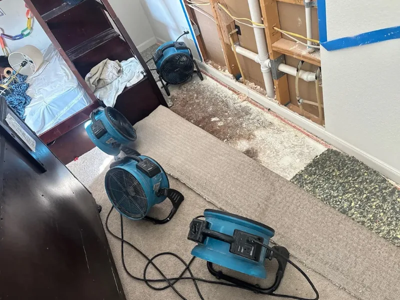Three blue air movers drying a room with a partially removed wall and carpet.